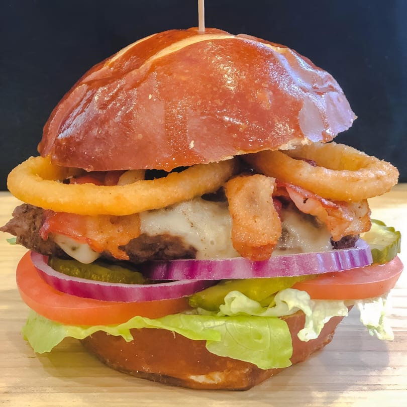 A Cappy's Pizza & Subs burger with bacon, onion rings, cheese, lettuce, tomato, onion, and pickles.