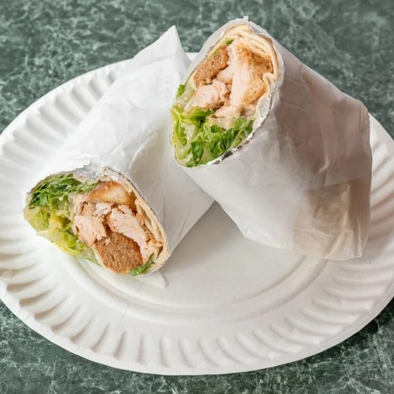 Two chicken and lettuce wraps, partially unwrapped, on a white paper plate.